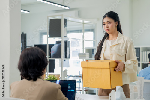 Bild auf Leinwand A woman sadly detaches her company phone from its lanyard strap while a colleague looks on, boxes of belongings nearby a quiet moment of returning corporate property during an office departure
