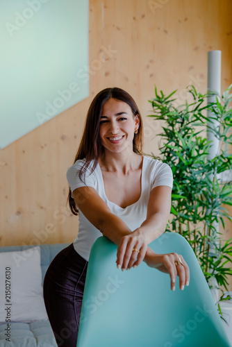 Foto Happy young woman laughing naturally while leaning over a turquoise chair in a b