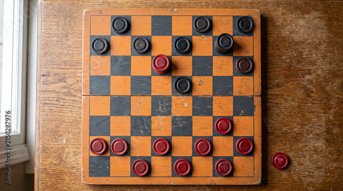 Top view of a wooden checkers board game with dark and red round pieces on a textured table