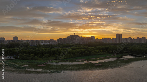 Fotografía Urban skyline rising beyond a green wetland park at sunrise