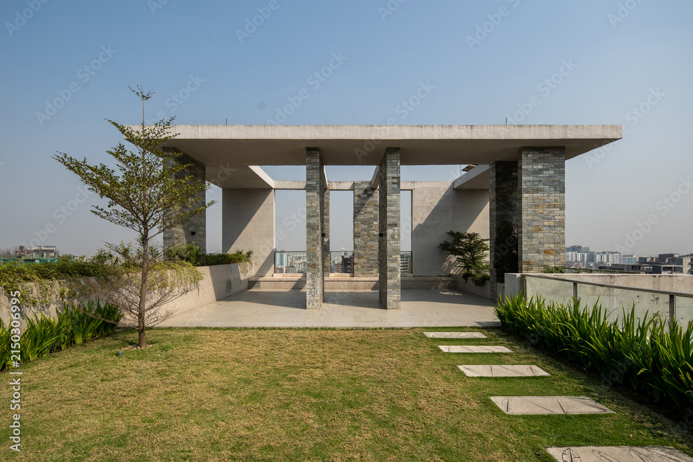 Fototapeta premium Modern Rooftop Garden with Open Pavilion, Stone Columns, Green Lawn, and Stepping Stone Pathway