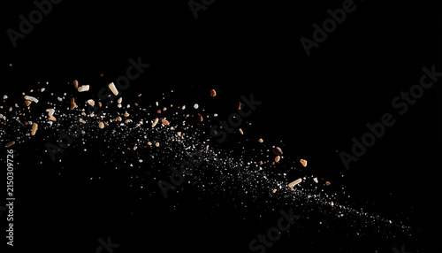 Scattered crumbs and particles of bread and grains suspended in mid-air against a stark black background, dynamic motion captured