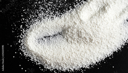 Close-up overhead view of fine white powder granules scattered on a dark black background surface creating a textured abstract pattern