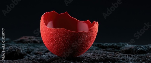 A cracked red eggshell rests on a dark, textured surface against a black background.