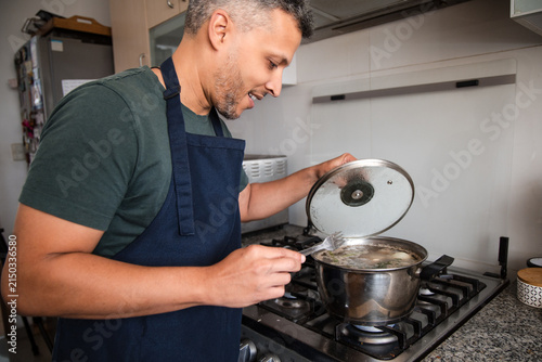 Smiling Man Lifting Lid of Simmering Pot in Kitchen