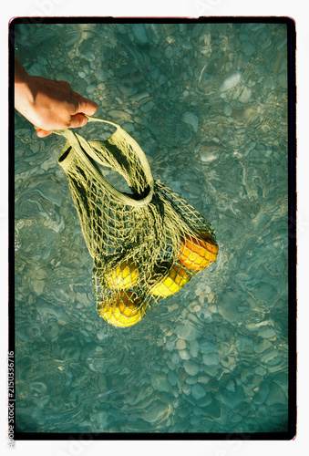 Lemons and oranges dangle in a mesh bag over the sea