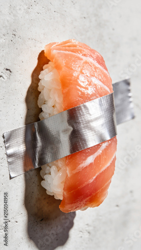 Sushi on light concrete background. Salmon nigiri duct-taped to a wall. Creative, modern, food art, safe packaging design concept. Japanese, oriental fusion restaurant menu, Vertical, close up