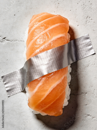 Sushi on light concrete background. Salmon nigiri duct-taped to a wall. Creative, modern, food art, safe packaging design concept. Japanese, oriental fusion restaurant menu, Vertical, close up
