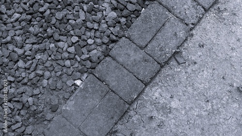 Monochrome ground surface combining crushed gravel, paving stones, and concrete, showing contrasting textures and geometric lines for construction and landscaping concepts.
