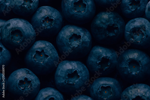 Close-up of fresh blueberries arranged in a dark, moody composition, highlighting their deep blue color, natural bloom and star-shaped crowns for a rich food photography background.