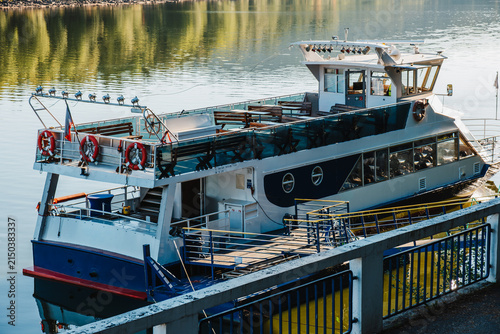 Foto Docked ferry with lifebuoys, open deck, gangway and calm lake reflections in warm summer light