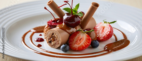 Chocolate dessert with cherries and strawberries on a white plate fruit pastry sweet treat confectionery roll strawberry cherry blueberry mint garnish sauce plated