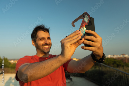 Man photographing solar eclipse with smartphone and solar filter