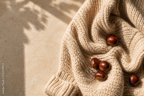 Cozy autumn composition with a soft knitted sweater, chestnuts and warm sunlight, featuring generous copy space for seasonal designs