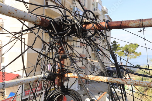 Urban infrastructure and power grid issues, tangled electrical wires and cables on a rusty pole in a city