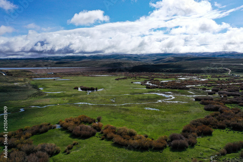 Dramatic 4K aerial video overlooking a sprawling Wyoming cattle ranch with a winding wild trout stream flowing through lush green pastureland. Expansive ranch country, wetlands, distant mountains, and