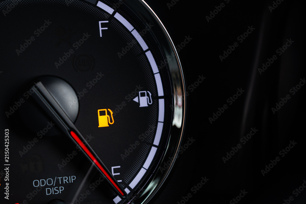 Fototapeta premium Fuel gauge with warning indicating low fuel tank on car dashboard
