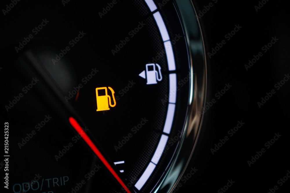 Naklejka premium Fuel gauge with warning indicating low fuel tank on car dashboard