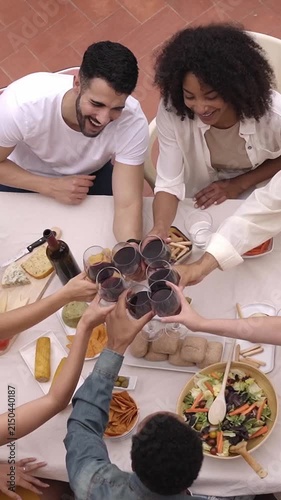 High angle view of people toasting. Happy group of Multiracial friends having dinner outside in a terrace celebrating with red wine. Vertical footage.