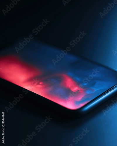 single unbranded smartphone lying on a black surface, screen showing an intentionally blurred generic human face without text, red and blue light