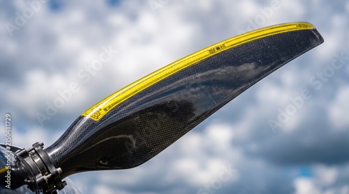 A detailed close up of a sleek carbon fiber airplane propeller blade against a bright blue sky.