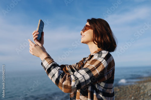 Bild auf Leinwand Woman holding a smartphone aloft by the seashore, capturing a moment with ocean