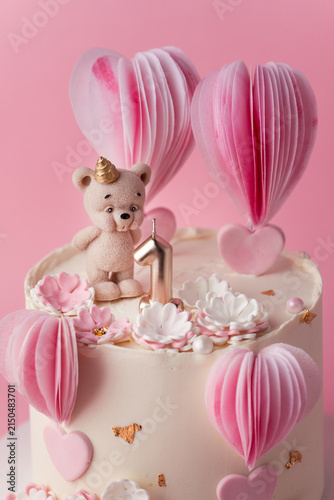 Pink hot air balloon themed birthday cake with teddy bear decoration. Cake for a one year old baby girl on the pink background