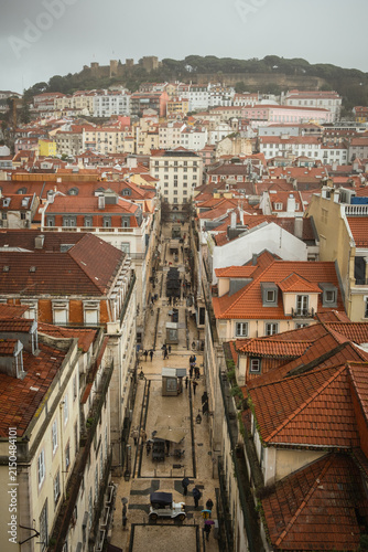 Panoramic view of Lisbon rooftops and steep streets in Portugal. Scenic urban landscape featuring historic architecture and dense city layout under cloudy skies.
