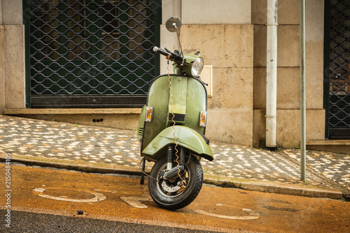 Vintage scooter parked on a rainy Lisbon street beside historic buildings. Atmospheric urban transportation scene capturing authentic Portuguese city life and travel mood.