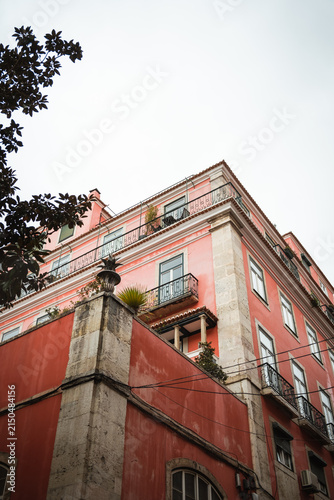 Pastel pink historic building facade in Lisbon photographed from a low angle, showcasing classic Portuguese architecture and decorative urban design on a cloudy day.