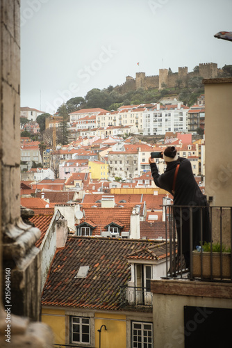 Traveler overlooking colorful Lisbon rooftops and historic neighborhoods in Portugal. Scenic city viewpoint capturing urban architecture and atmospheric European travel experience.