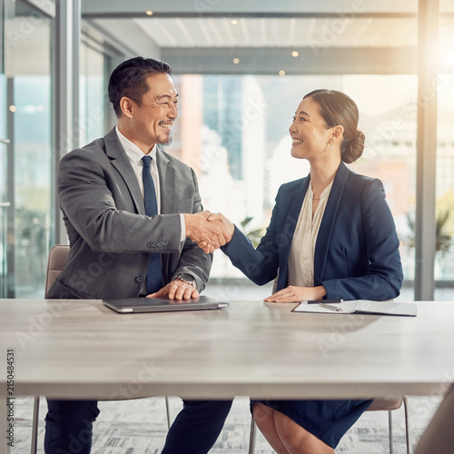 Two Japanese business professionals shaking hands after successful deal in office