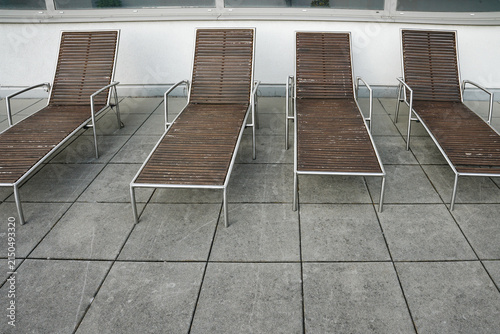 Row of empty modern wooden deck chairs on outdoor concrete tile terrace