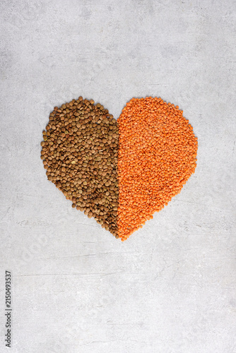 Heart shape made of brown and red lentils on gray background. Healthy food concept, vertical top view.