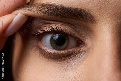 Close up of a young woman pulling her upper eyelid skin with fingers to evaluate drooping skin before plastic surgery for eye rejuvenation. Blepharoplasty preparation and eyelid lift concept