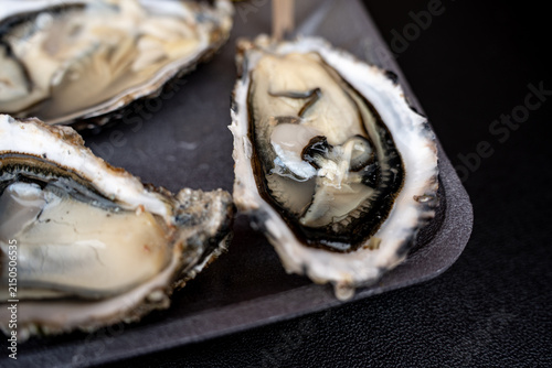 Fresh opened oysters on a black tray served with a slice of lemon and a wooden toothpick on a dark background.