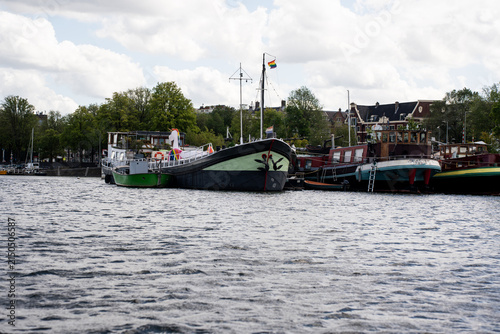 Historic barges and houseboats with an LGBT pride flag moored on the Amstel river in Amsterdam, Netherlands.