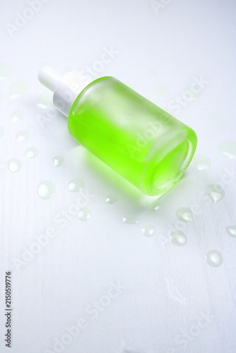 Green Facial Serum Glass Dropper Bottle Surrounded By Serum Drops On White Surface