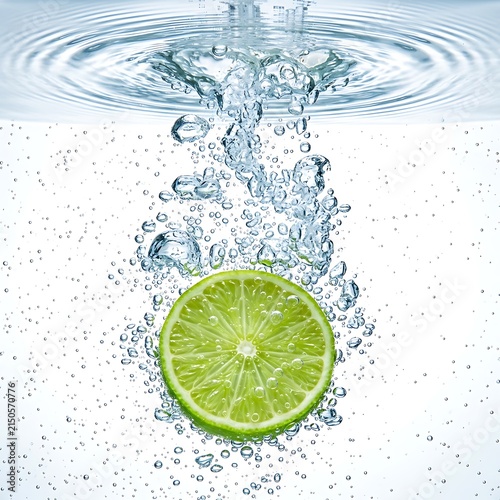 Fresh green lime slice submerged in clear water with air bubbles and surface ripples