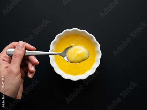 Close-up of a hand holding a silver spoon with a dollop of yellow clarified butter over a bowl of melted ghee