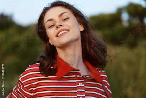 Quadro su tela A smiling young woman in a striped polo shirt enjoys the warm sunlight outdoors