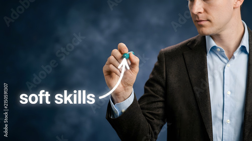Professional man in a dark suit and light blue shirt draws an upward arrow with a green marker next to the text soft skills on a dark background featuring businessman, blazer, drawing and writing