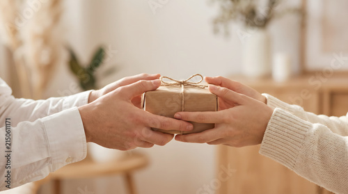 Close-up of two people's hands exchanging a rustic wrapped gift box tied with twine. Represents giving, celebration, and thoughtful gestures