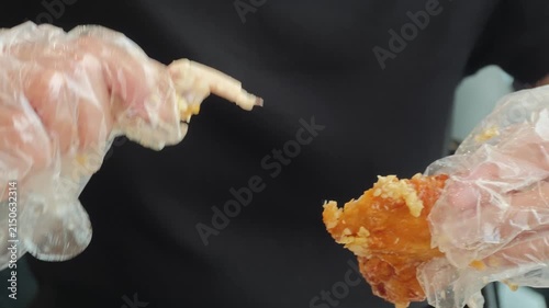 Young woman wearing disposable plastic gloves biting into a crispy garlic fried chicken wing, close up of her mouth and hands while eating