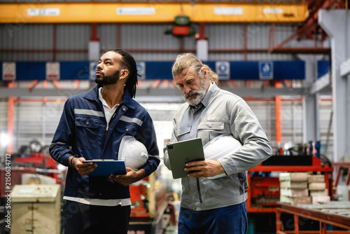 Senior factory manager guiding a young worker during an inspection. Analyzing production data on a tablet. Teamwork and leadership in an industrial business. Making an inspection together with team.