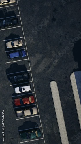 In a parking lot, several cars are parked in marked spaces. Some parking spots are empty. The scene shows a variety of colored vehicles in organized rows.