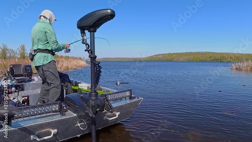 Unrecognizable man casting rod and spinning fishing reel on small fishing boat. Sport fishing leisure. Man is fishing in a boat on the lake. Angler is catching fish from powerboat in the open water.