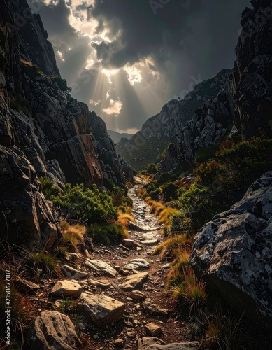 A rugged mountain path bathed in dramatic sunbeams breaking through stormy clouds.