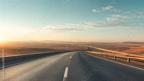 Scenic open desert highway stretching into distant horizon under soft warm sunset sky with smooth curved asphalt road and safety guardrails
