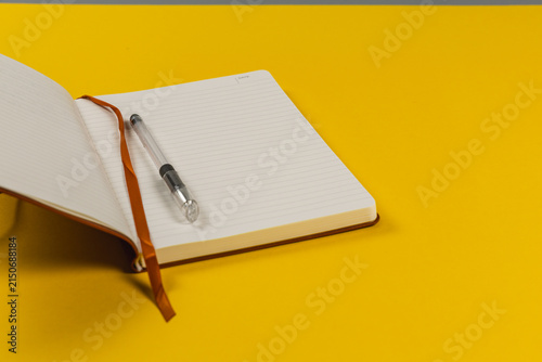 Notebook and pen on workspace with bright yellow background